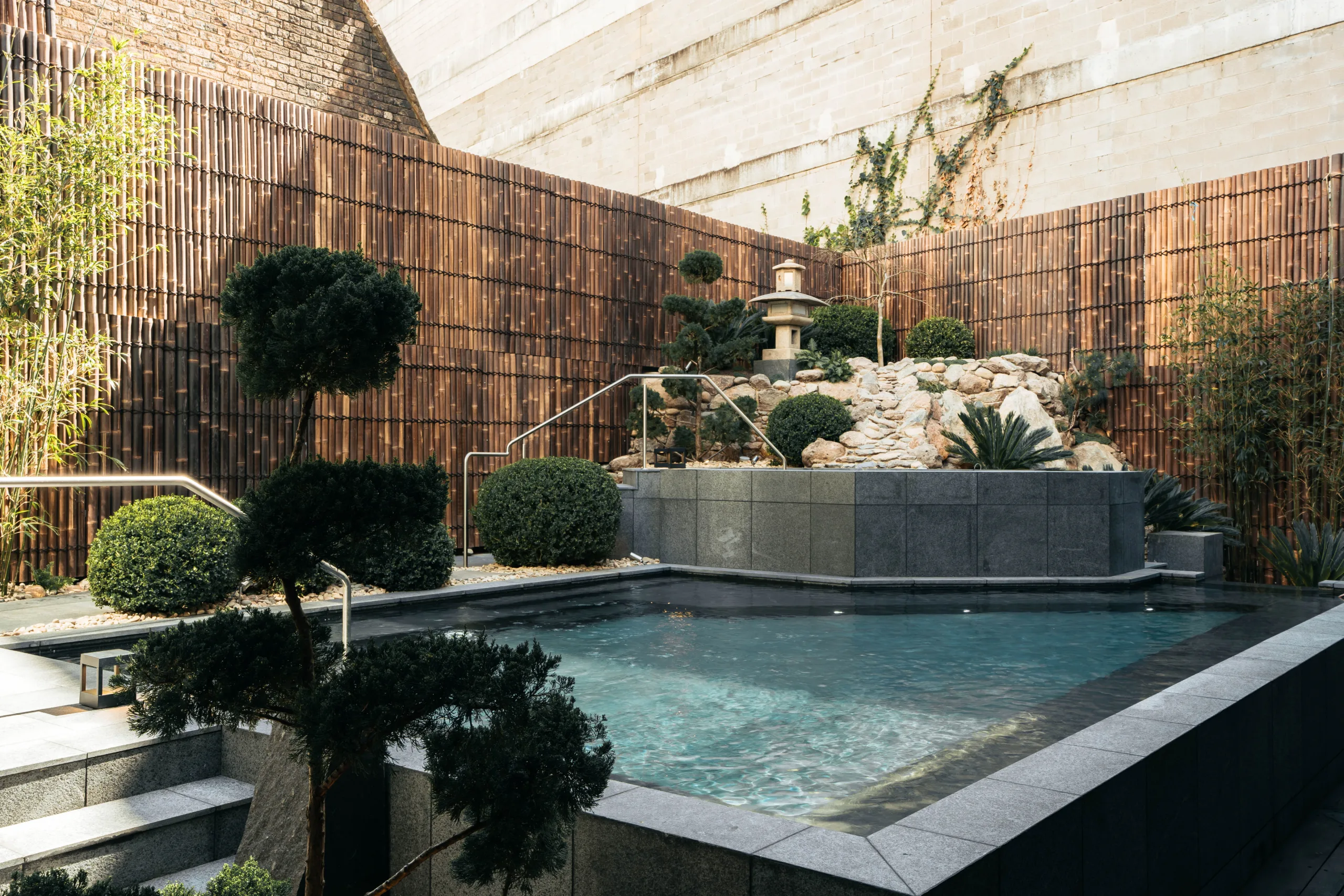 Outdoor onsen bathing pool at ONSEN Sydney framed by a bamboo screen, cloud-pruned trees and a stone lantern garden